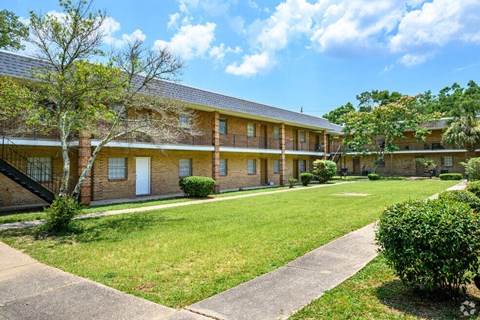 the front of a brick apartment building with a lawn and sidewalk