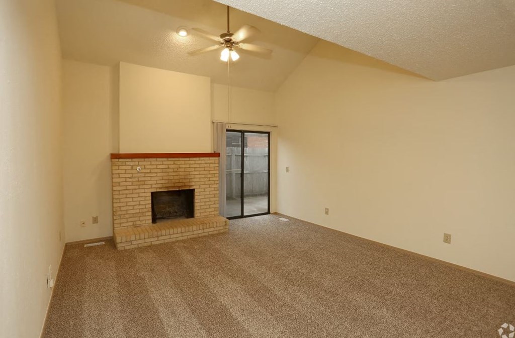 an empty living room with a fireplace and a ceiling fan
