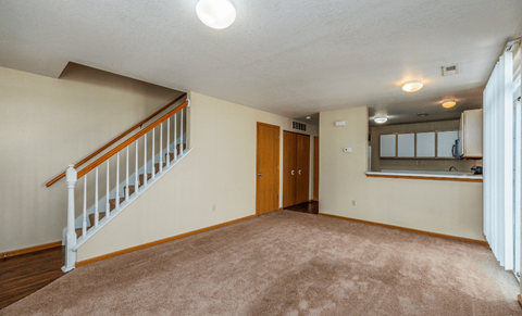 an empty living room with a staircase and a door to a kitchen