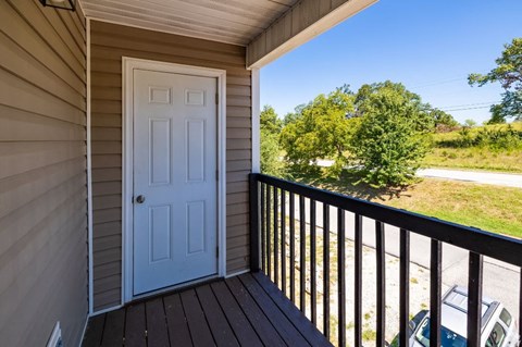 a white door opens to a balcony with a blue sky and trees in the background