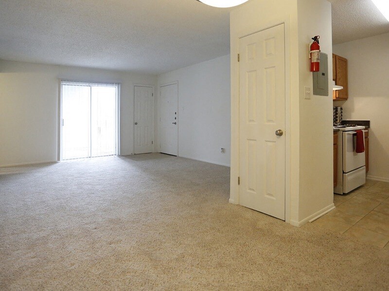 an empty living room with a kitchen in the background