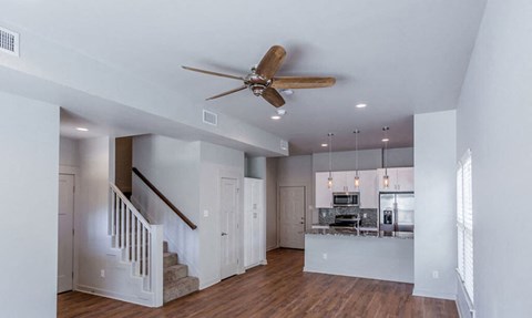 A spacious living room with a staircase and a ceiling fan.