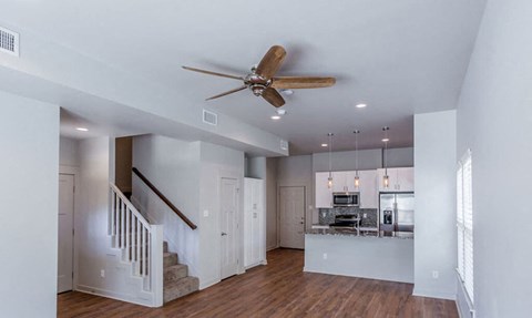 A spacious living room with a staircase and a ceiling fan.