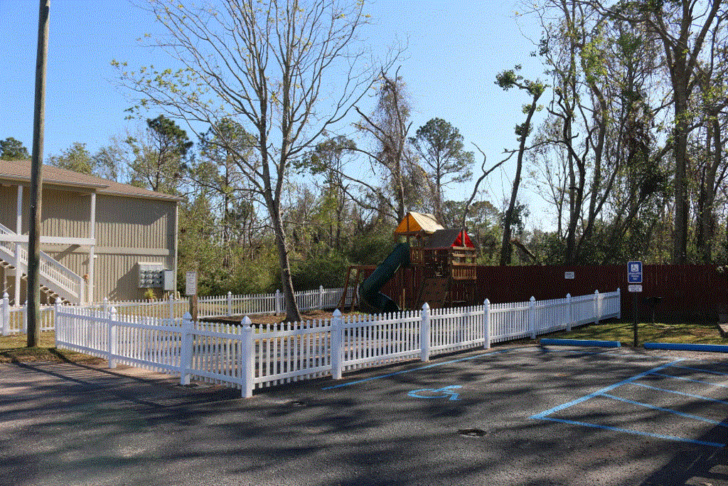 a view of a playground and a white picket fence in front of a house