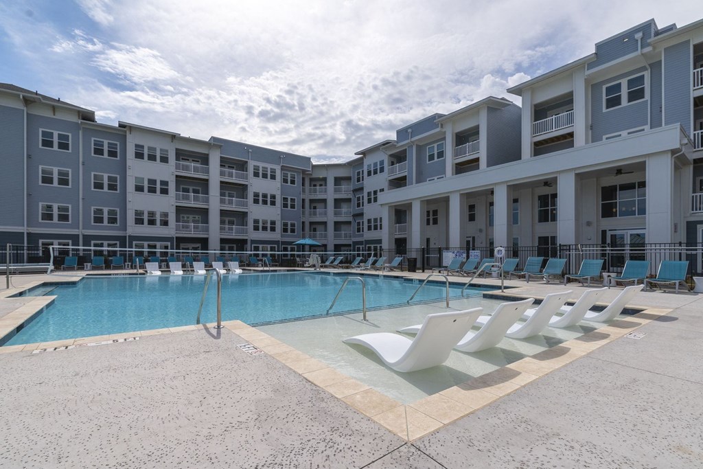 a swimming pool with chaise lounge chairs and a building in the background