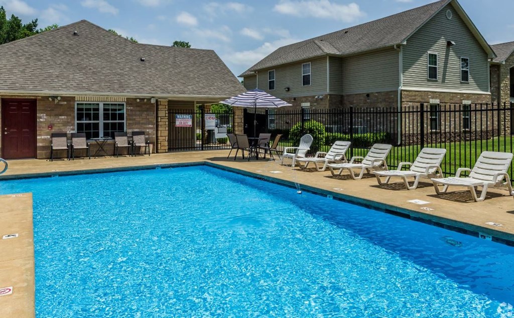 a swimming pool with chaise lounges and umbrellas in front of a house