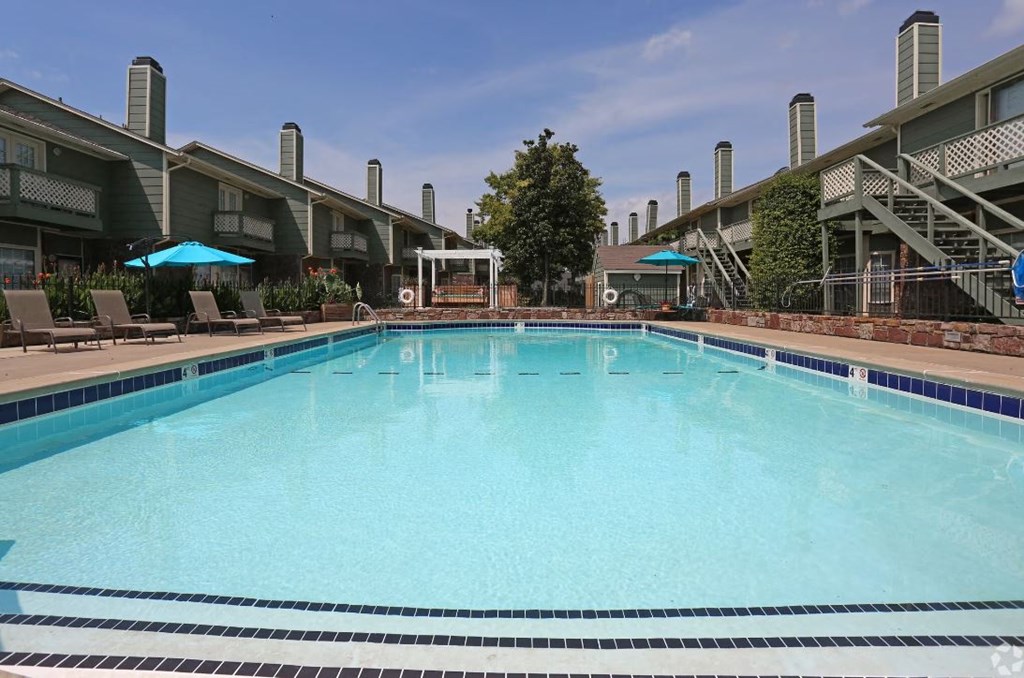a large swimming pool with lounge chairs and umbrellas in front of a building