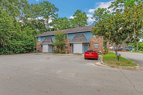 a red car parked in a parking lot in front of a brick house
