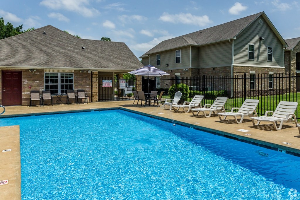 a swimming pool with chaise lounges and umbrellas in front of a house