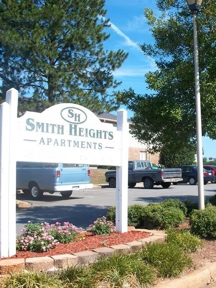 A sign for Smith Heights Apartments is in front of a parking lot.