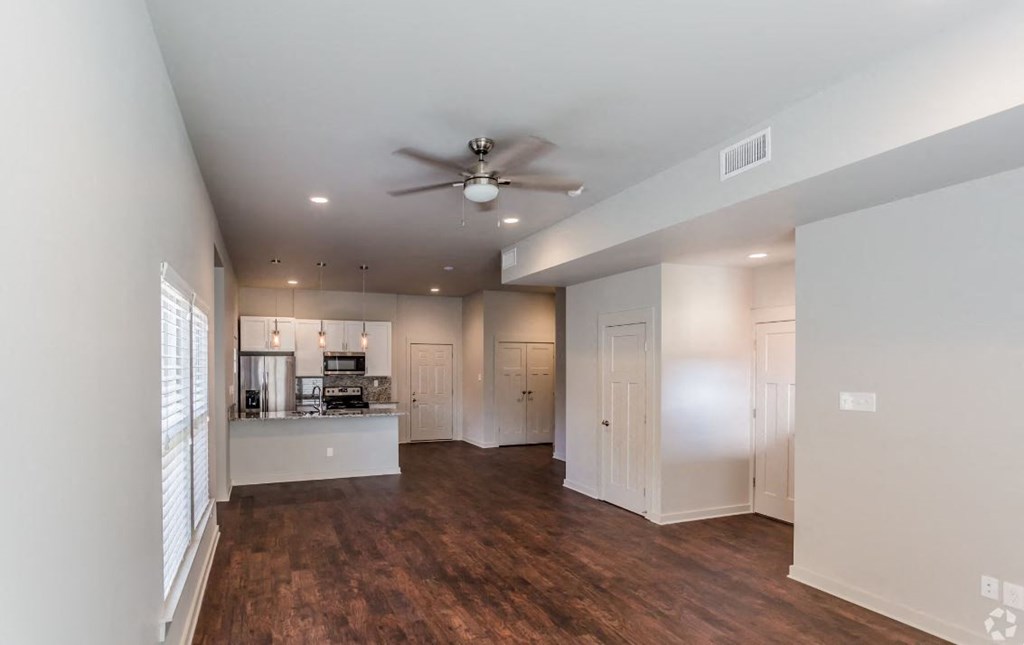 a living room with a ceiling fan and a kitchen in the background