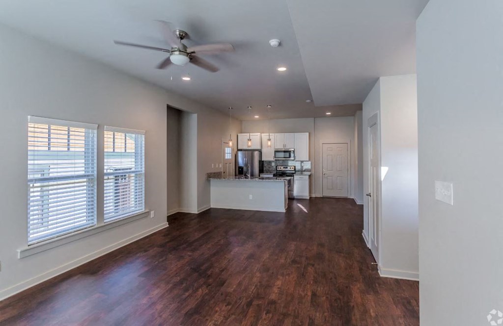 a living room with a ceiling fan and a kitchen in the background