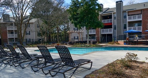 A row of black lounge chairs are arranged on a concrete patio next to a pool.