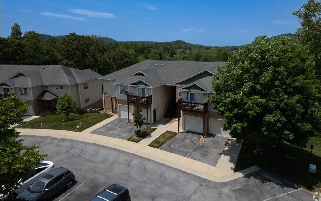 an aerial view of a tan house with a gray roof and a green hillside in the