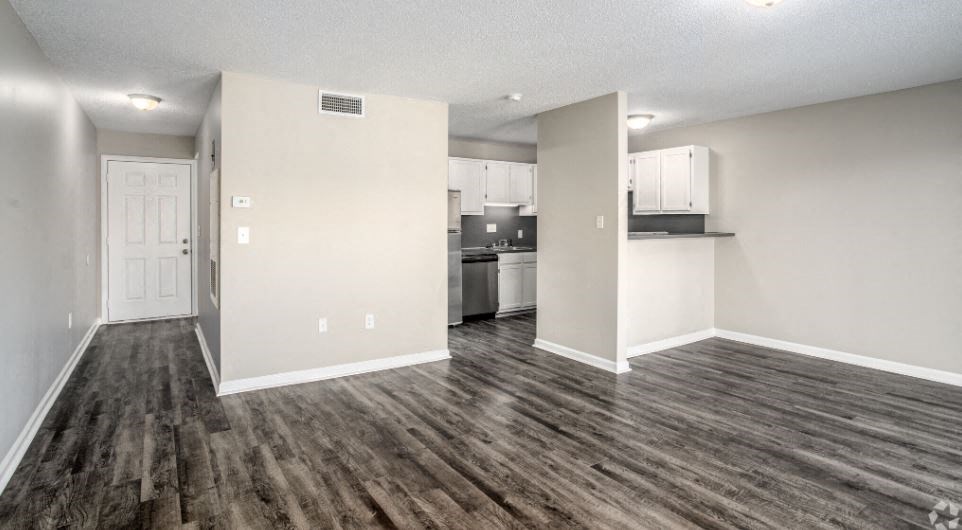 an empty living room with a kitchen in the background