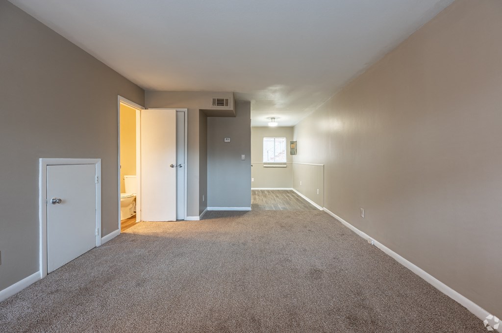 an empty living room with carpet and a door into a bedroom