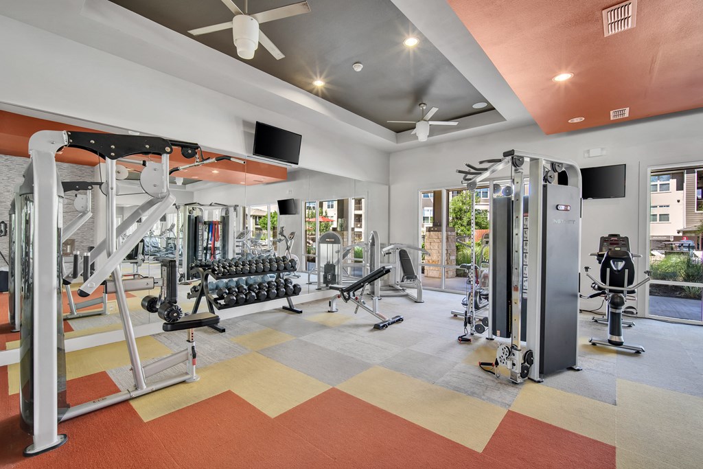 a gym with a lot of weights and cardio equipment and a ceiling fan