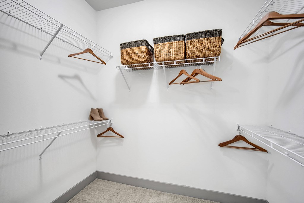 a walk in closet with white walls and shelves with baskets and hangers