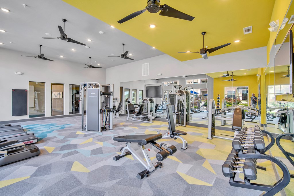 a gym with weights and cardio equipment and a ceiling fan