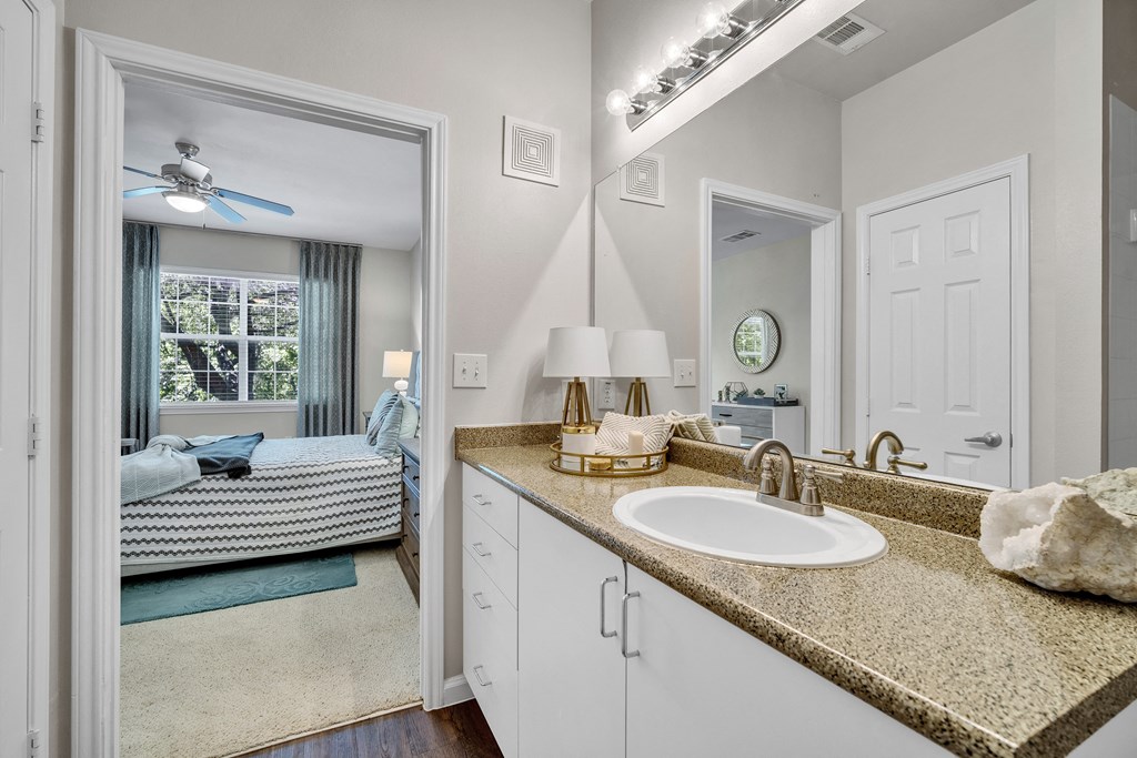 a bathroom with a sink and a mirror and a door to a bedroom