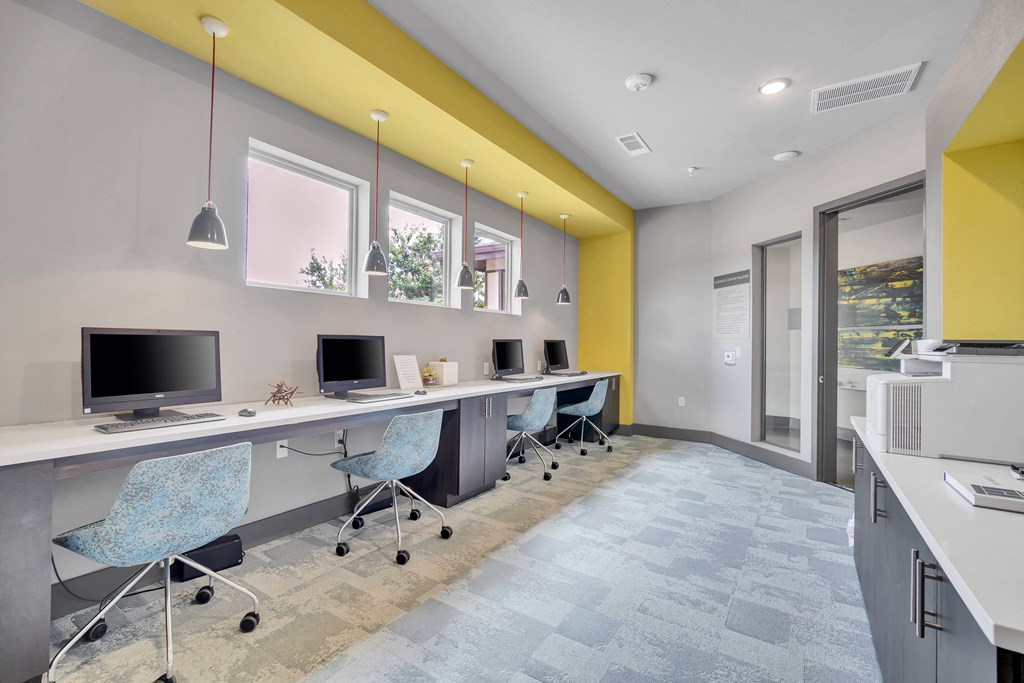 a long desk with computers and chairs in a room with a yellow wall
