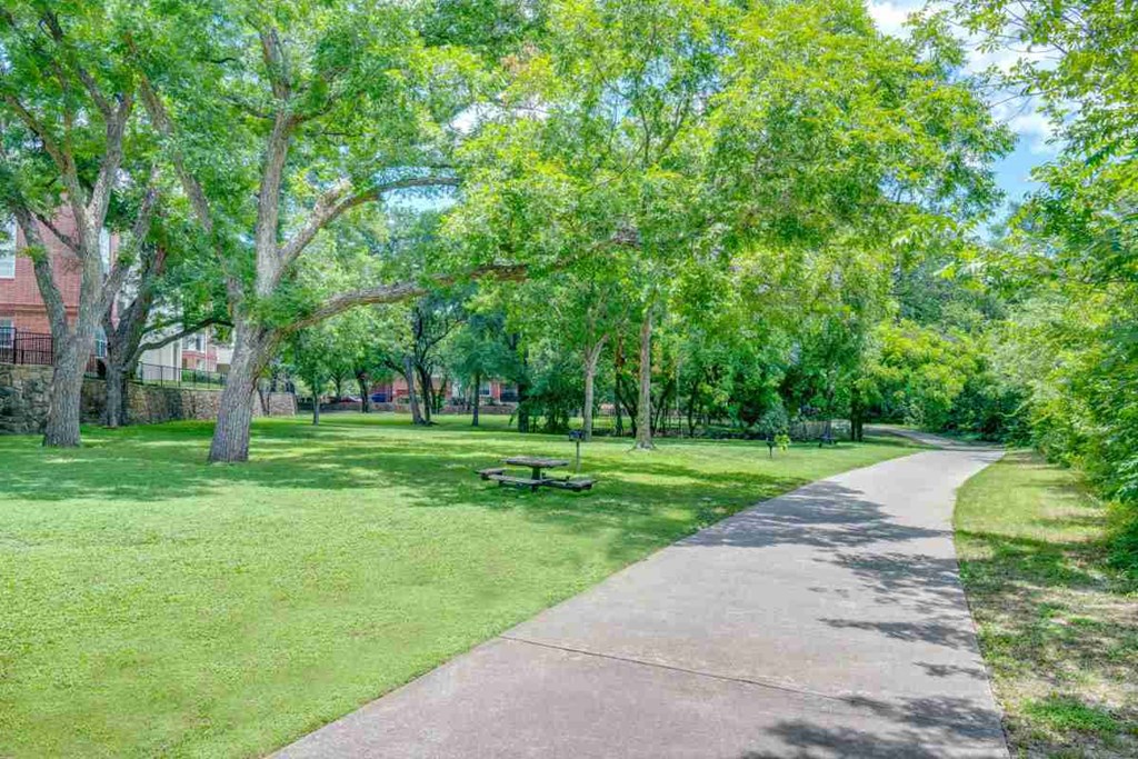 a sidewalk through a park with trees and a picnic table