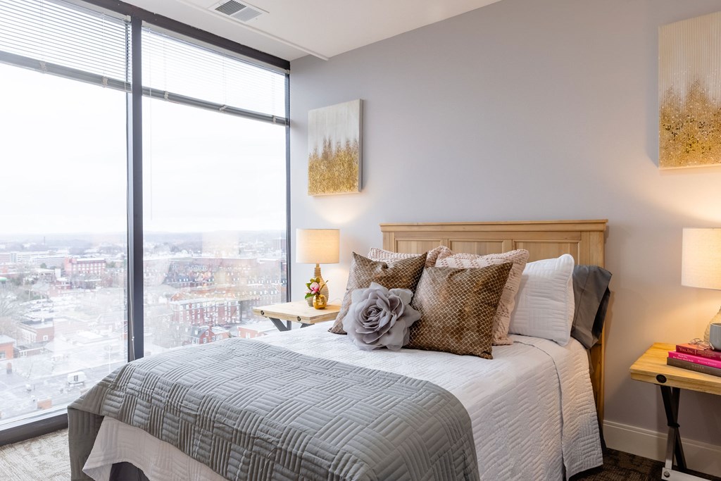 A bedroom with a large window overlooking a cityscape.