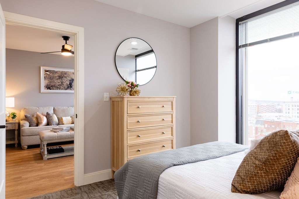 A bedroom with a bed, dresser, and a round mirror on the wall.