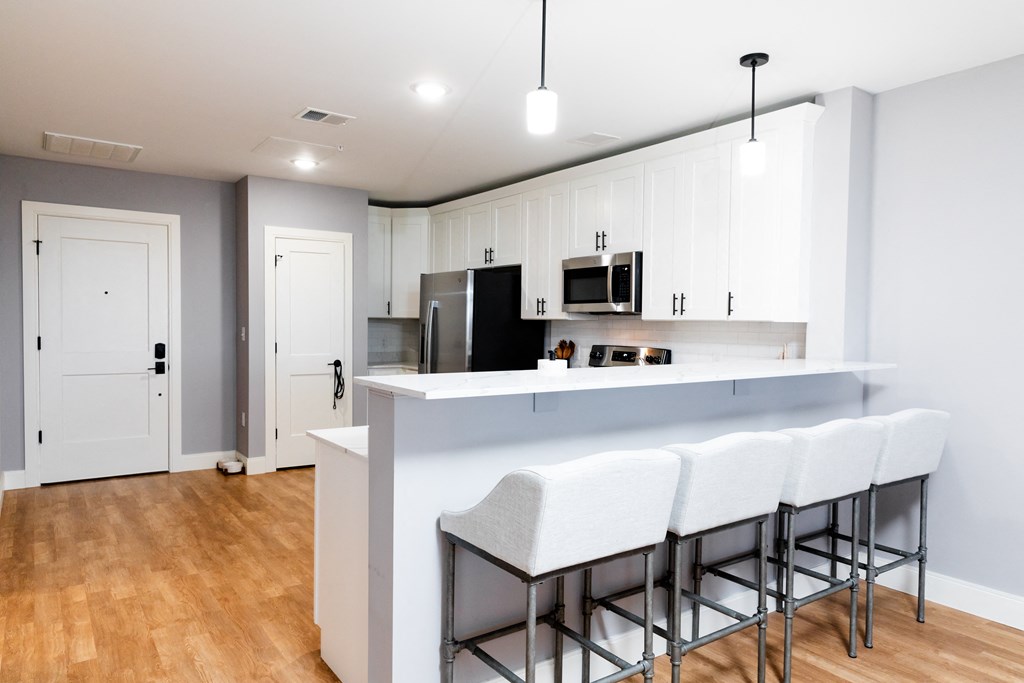 a kitchen with white cabinets and a white counter top with three stools in front of it
