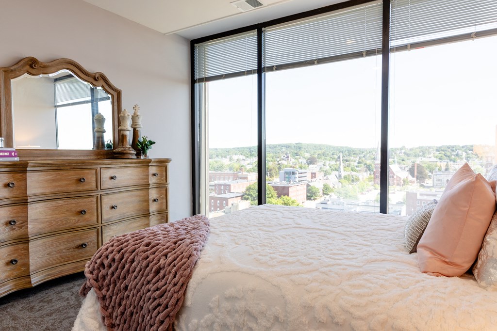 a bedroom with a large window and a dresser with a mirror