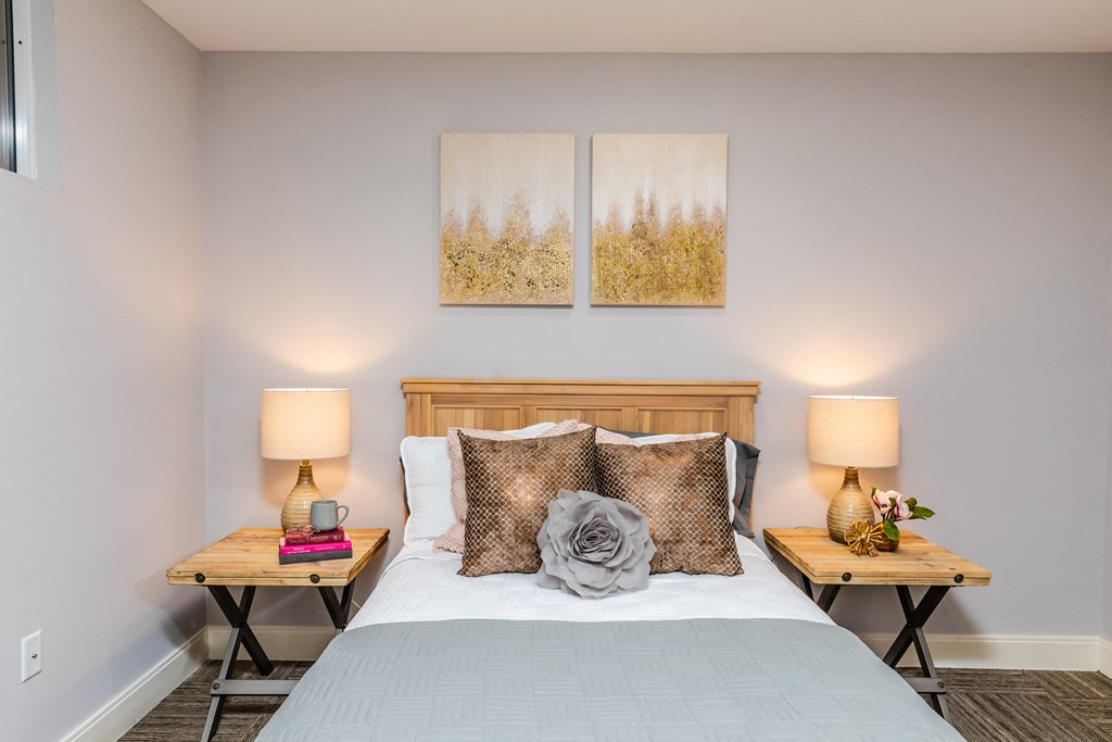 a bedroom with a bed two night stands and two paintings on the wall