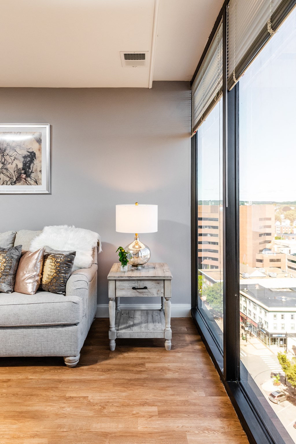 a living room with a gray couch and a table with a lamp and a large window