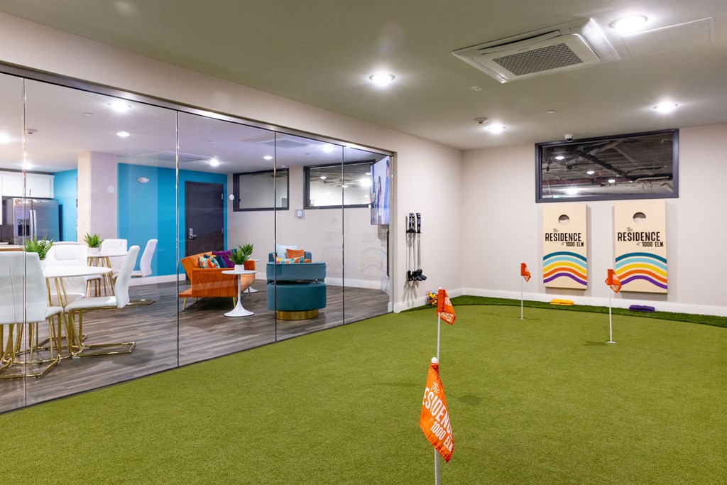 a room with an indoor putting green and a conference room with glass walls