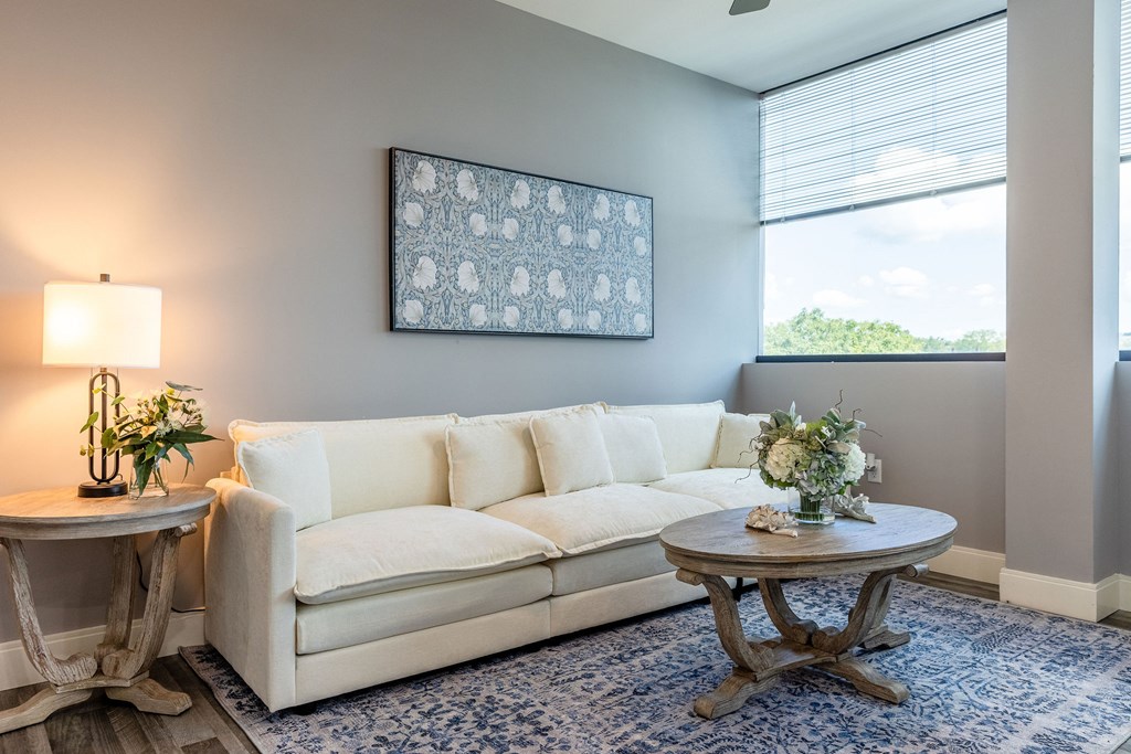 A living room with a white couch, a round table with a vase of flowers, and a framed picture on the wall.