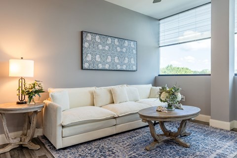 A living room with a white couch, a round table with a vase of flowers, and a framed picture on the wall.