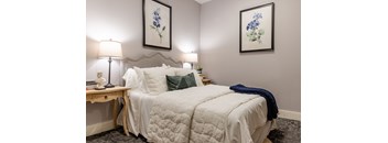 A bedroom with a bed, two lamps, and two framed pictures on the wall.