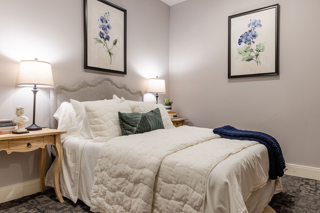 A bedroom with a bed, two lamps, and two framed pictures on the wall.