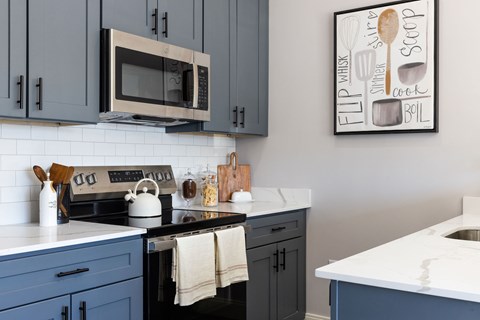 A kitchen with a white counter top and a picture of a whiskey glass and a spoon on the wall.