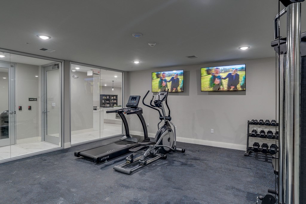a home gym with exercise equipment and two televisions on the wall