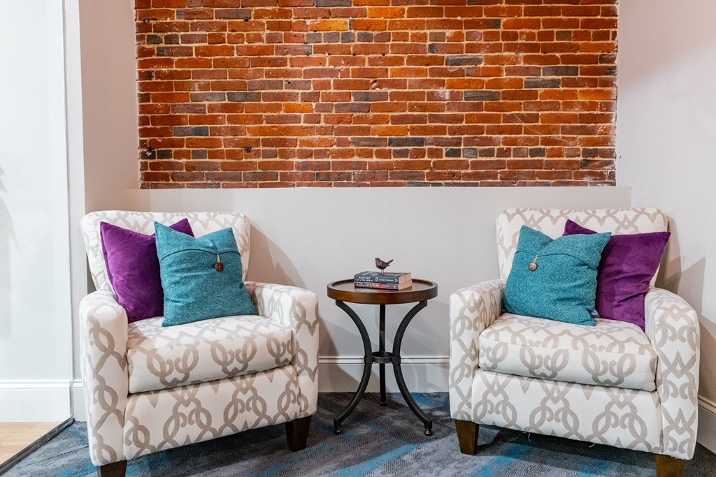 two chairs with pillows in front of a brick wall