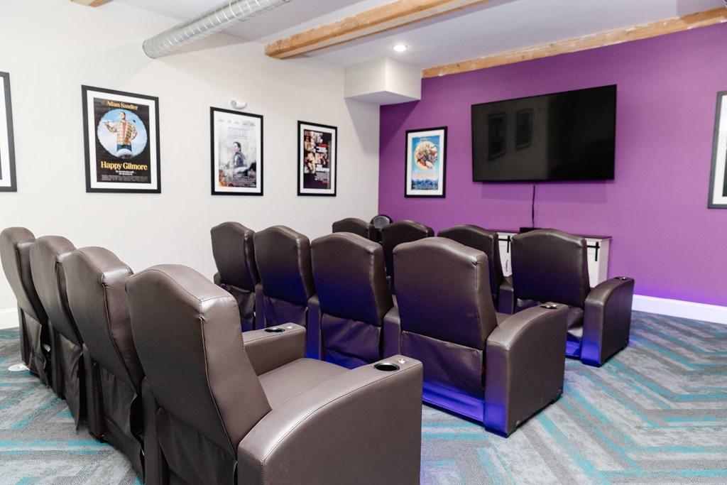 a theater room with purple walls and leather chairs and a tv