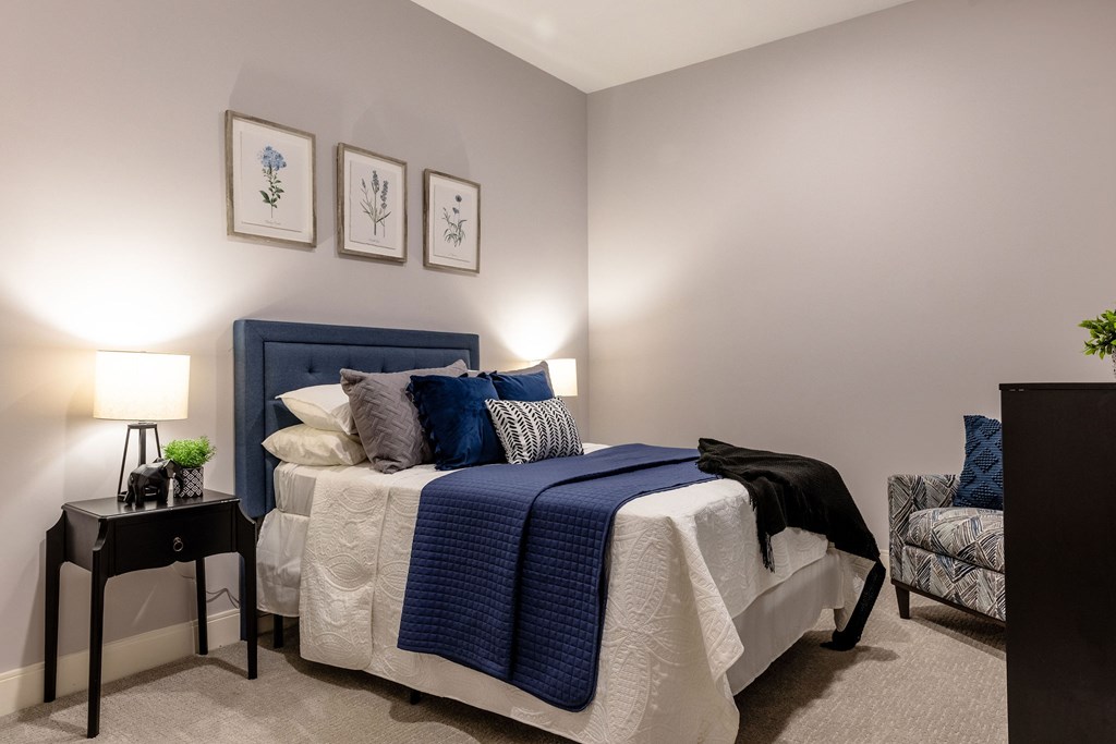 A bedroom with a bed, a nightstand, and a chair.