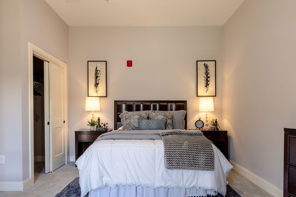 A bedroom with a large bed and two wall lamps.