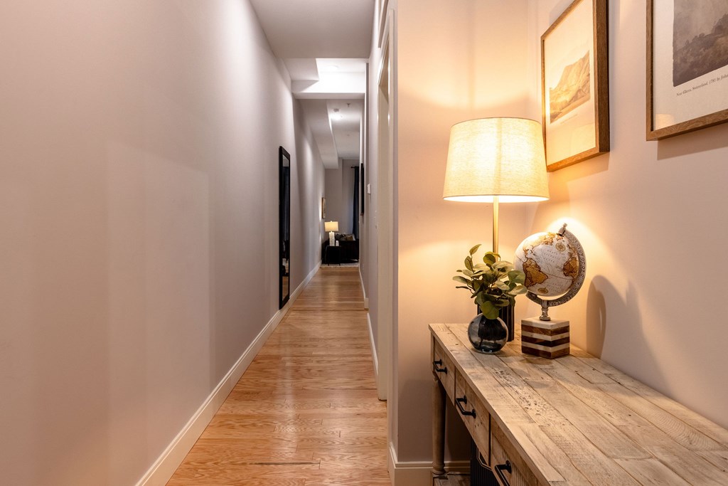 A hallway with a wooden floor and a lamp on a table.