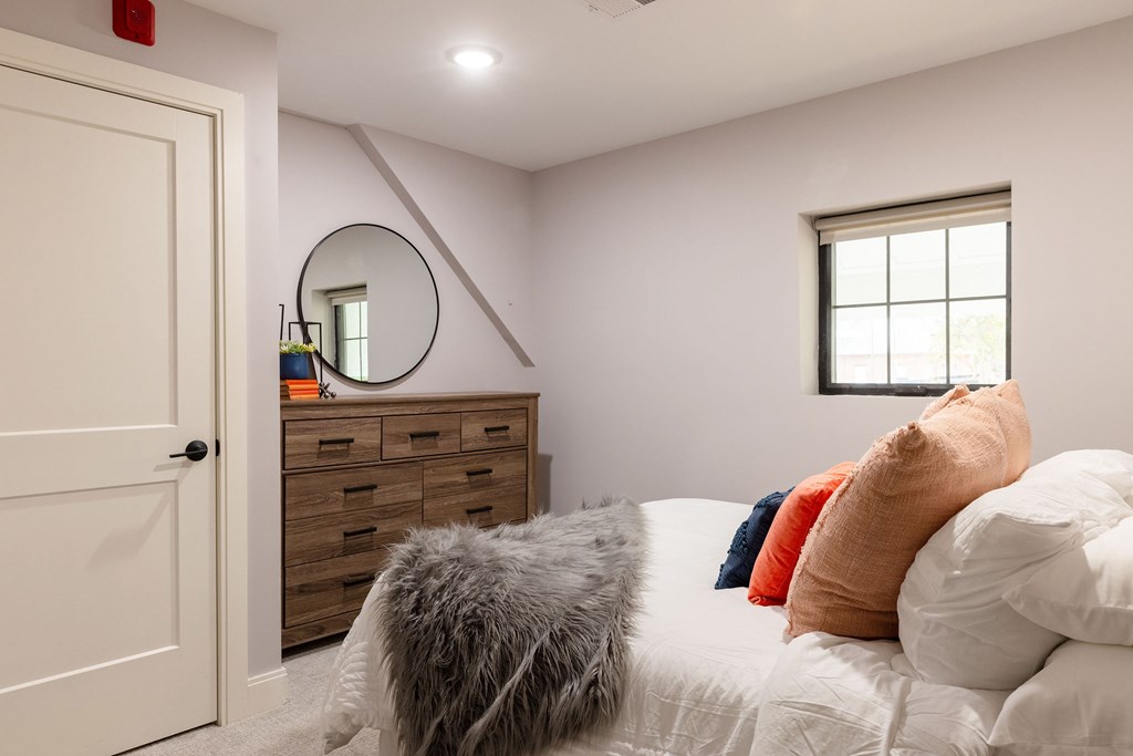 A bedroom with a bed, pillows, a dresser, and a mirror.