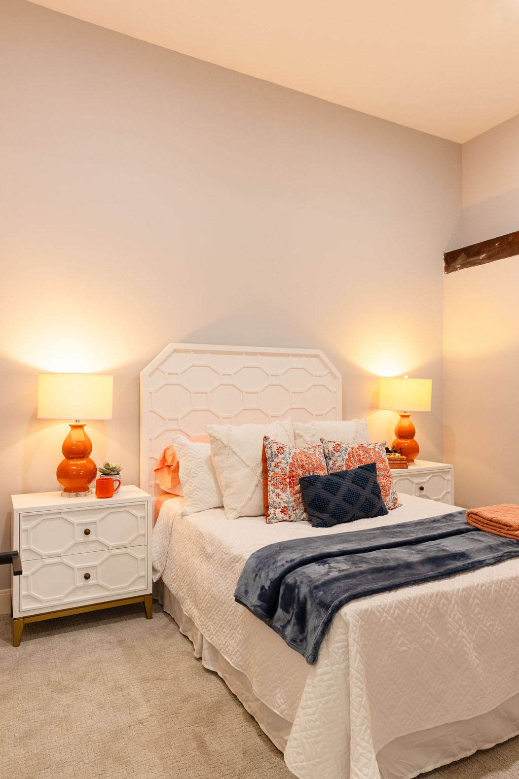A bedroom with a white bed and a white nightstand with two orange lamps.