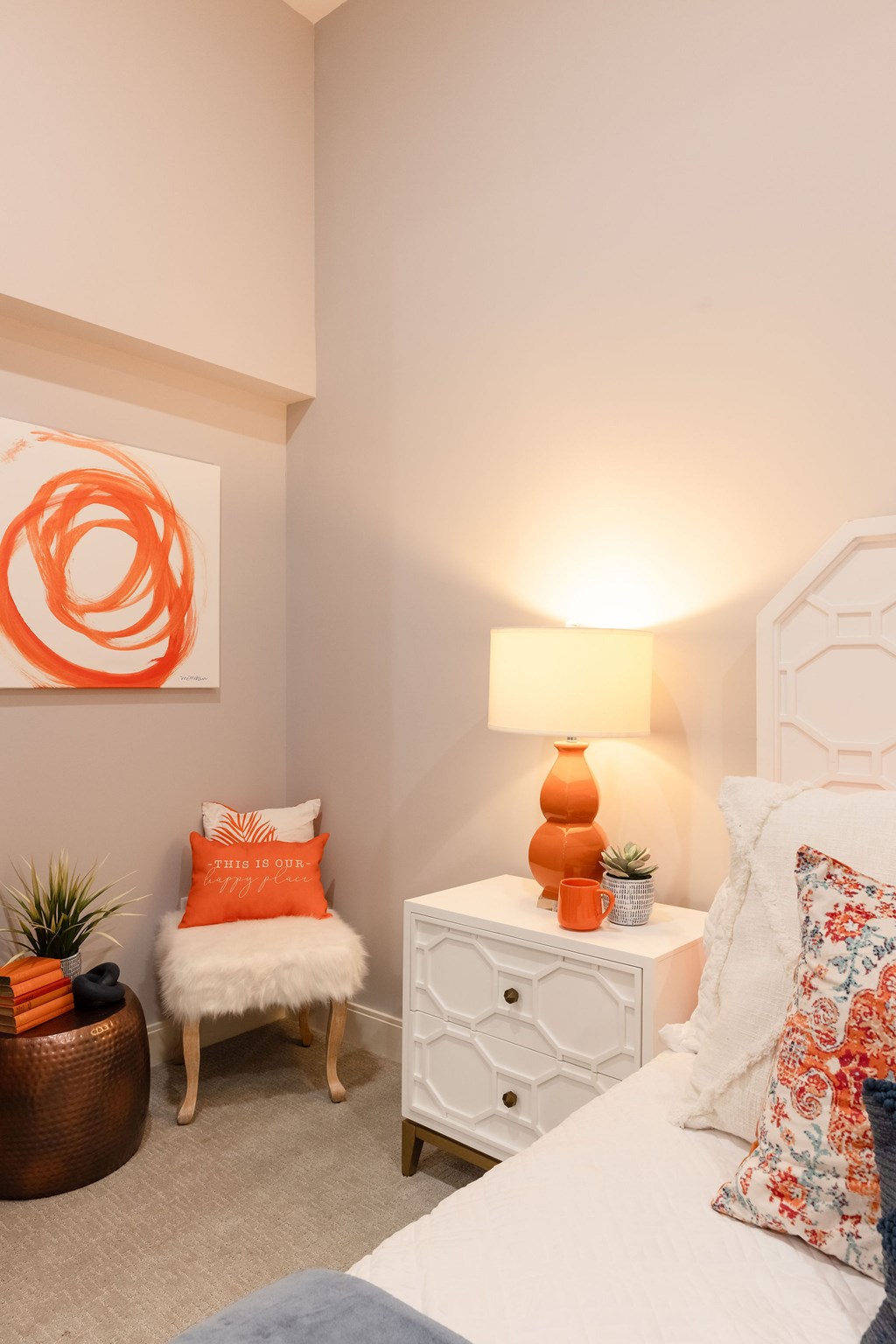 A bedroom with a white bed, a white nightstand with a lamp, a chair, and a painting on the wall.