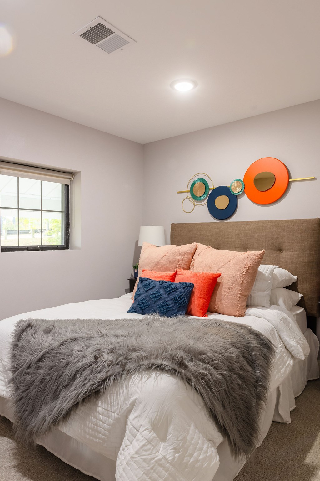 A bedroom with a bed covered in a grey fur throw and a wall art of circles.