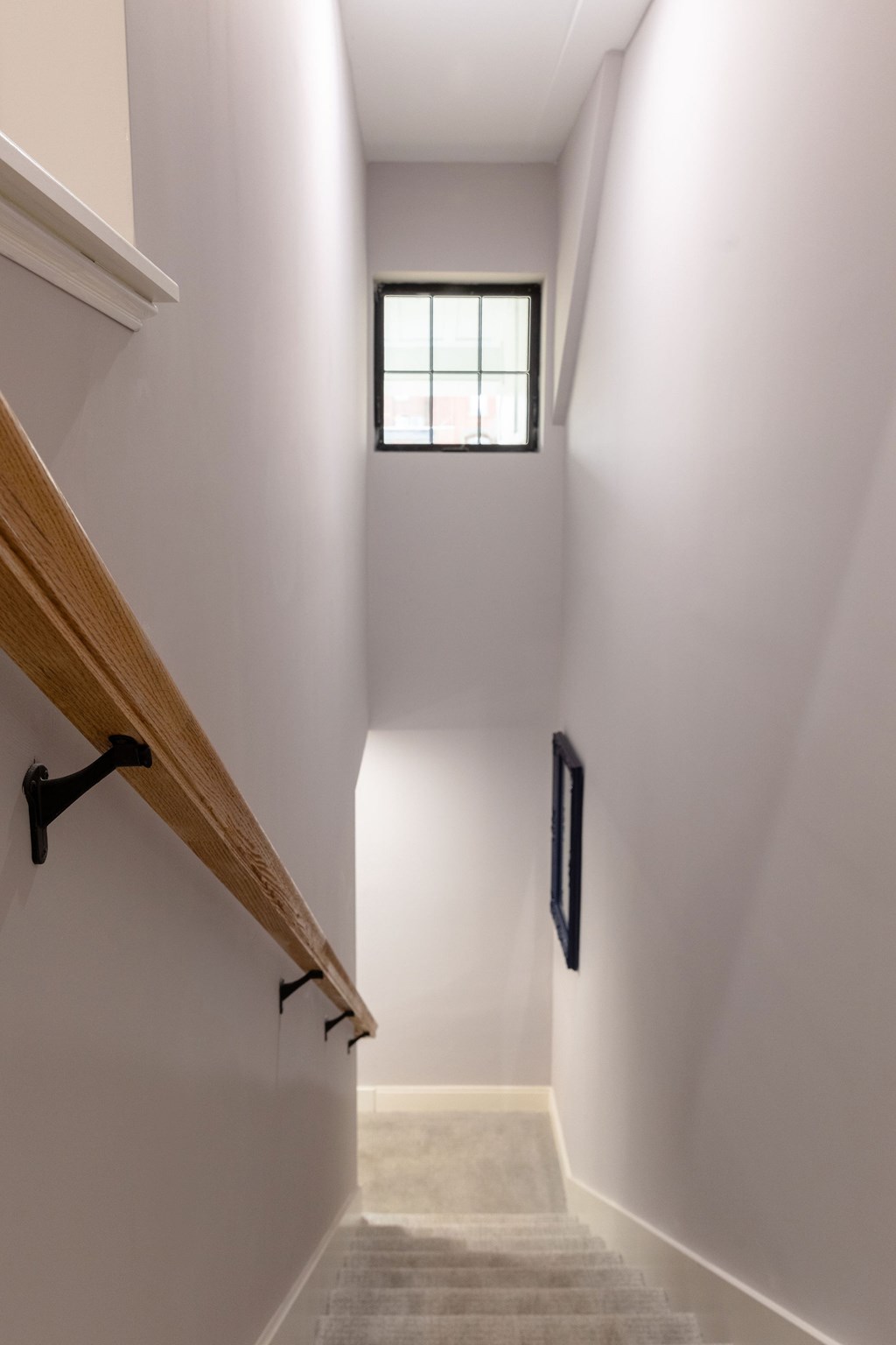 A stairway with a light brown wooden handrail and white steps.