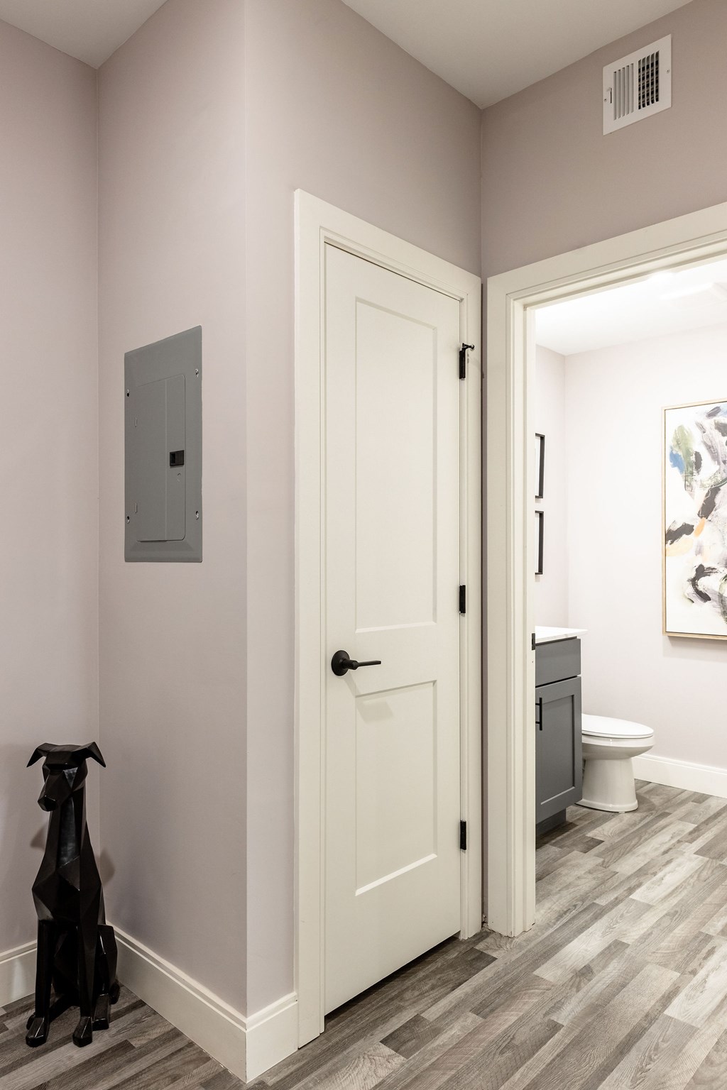 A black dog is standing in a hallway next to a white door.